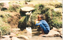 Young child collecting water from spring in rural Africa